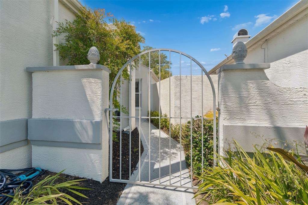 A white metal arched gate stands between two stucco pillars leading to a paved walkway — 10491 CASA GRANDE CIRCLE, SPRING HILL, FL