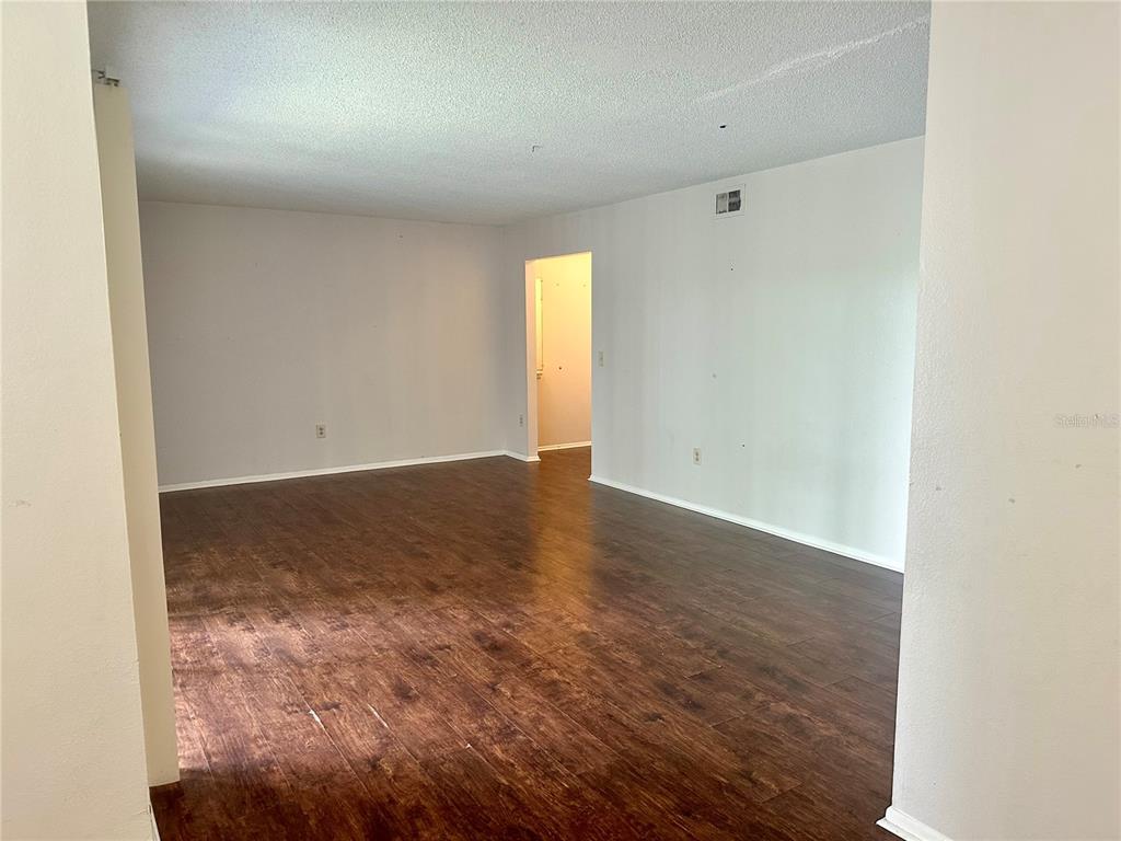 An empty room features dark wood-look flooring, white walls, and a doorway leading to another area — 3992 VERSAILLES DRIVE UNIT 3992C, ORLANDO, FL