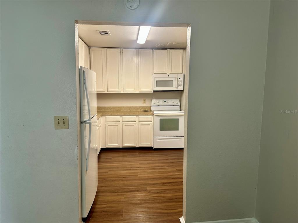 A kitchen with white cabinets, white appliances, and wood-look flooring viewed through a doorway — 3992 VERSAILLES DRIVE UNIT 3992C, ORLANDO, FL