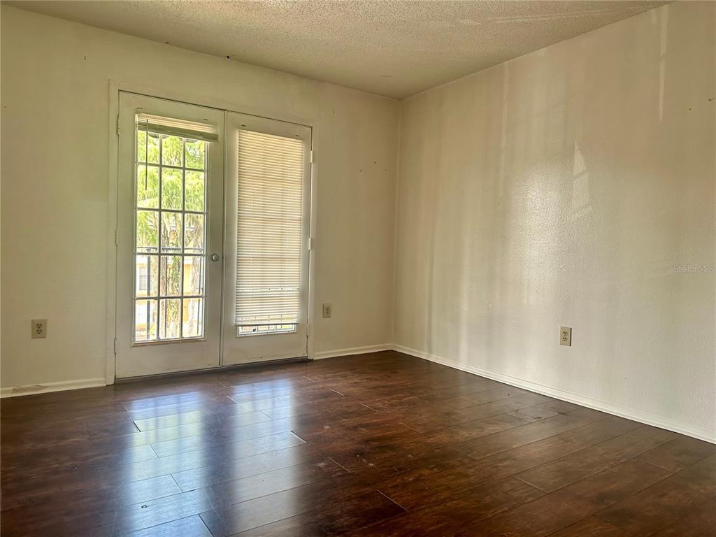 An empty room features dark wood-look flooring, white walls, and a glass-paned double door — 3992 VERSAILLES DRIVE UNIT 3992C, ORLANDO, FL