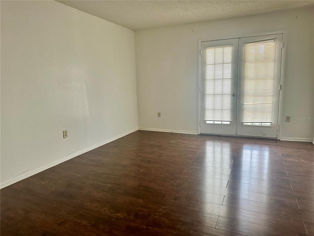 An empty room features dark wood-look flooring, white walls, and a set of glass French doors — 3992 VERSAILLES DRIVE UNIT 3992C, ORLANDO, FL