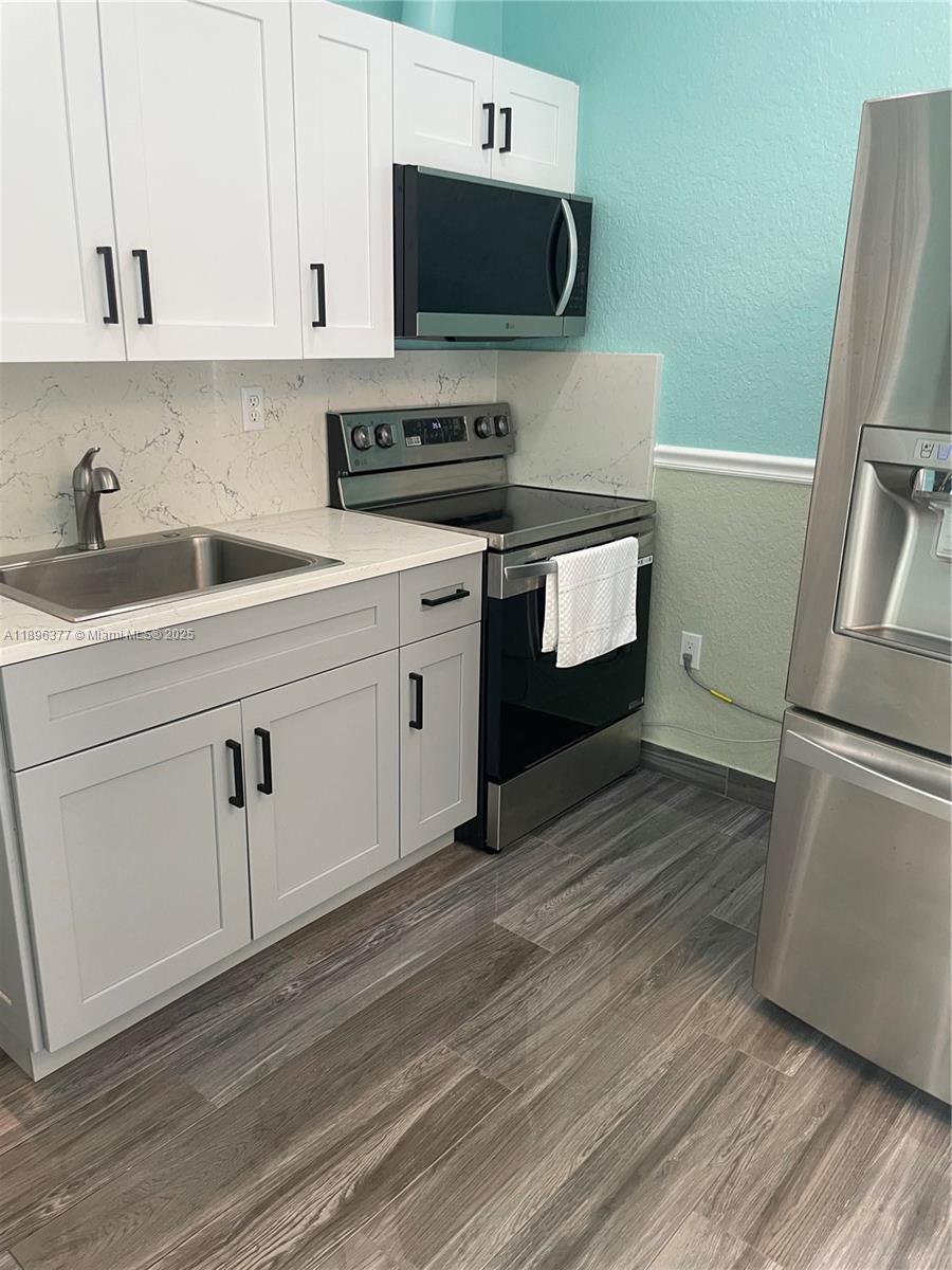 A kitchen features white upper cabinets, gray lower cabinets, stainless steel appliances, and wood-look flooring — 240 NE 27th St # 1, Pompano Beach FL 33064, POMPANO BEACH, FL