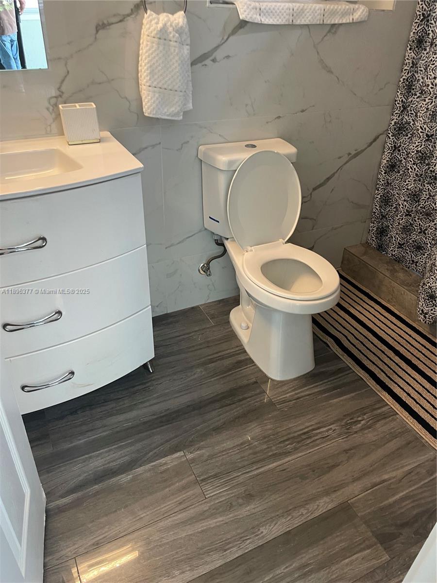 A bathroom features a white vanity, a toilet, and gray wood-look tile flooring — 240 NE 27th St # 1, Pompano Beach FL 33064, POMPANO BEACH, FL