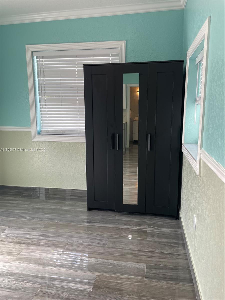 A room with two-toned walls, wood-look tile flooring, and a black three-door wardrobe — 240 NE 27th St # 1, Pompano Beach FL 33064, POMPANO BEACH, FL