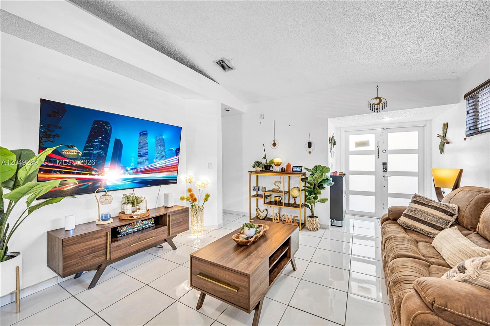 A living room features white tile floors, a large wall-mounted television, and brown furniture — 7256 W 34th Ln, Hialeah FL 33018, HIALEAH, FL