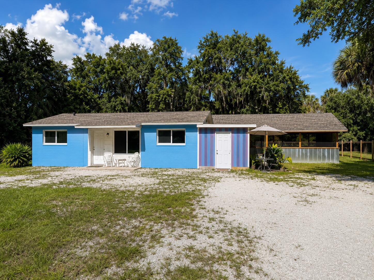 A single-story blue house with a gravel driveway, a striped accent wall, and a screened porch — 8012 U.s. 1, Vero Beach FL 32967, VERO BEACH, FL
