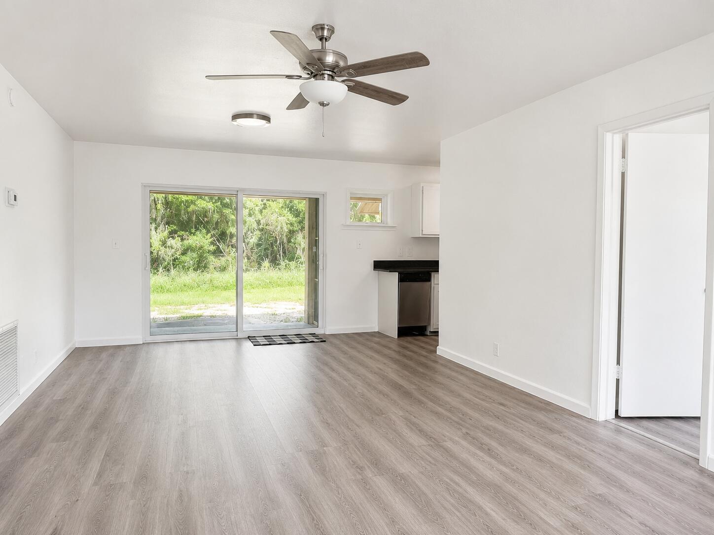 An empty living room with light wood-look flooring, a ceiling fan, and a sliding glass door — 8012 U.s. 1, Vero Beach FL 32967, VERO BEACH, FL