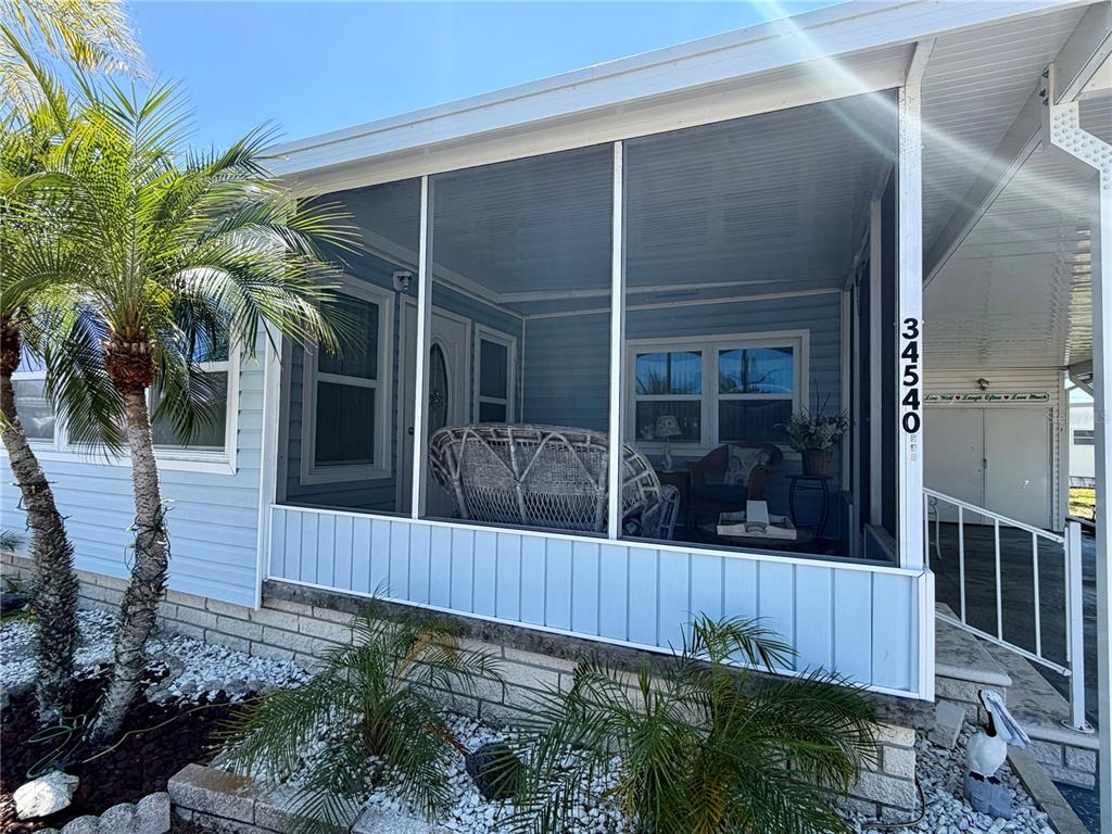 A light blue mobile home features a screened-in front porch with white trim and landscaping — 34540 VIOLET DRIVE N, PINELLAS PARK, FL