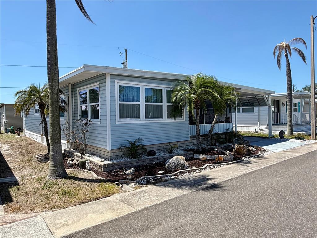 A light blue mobile home with a carport and palm trees sits on a street — 34540 VIOLET DRIVE N, PINELLAS PARK, FL