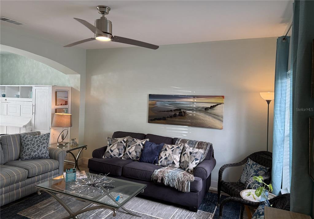 A living room features a dark sofa, a glass coffee table, and a ceiling fan — 3304 LISA LANE UNIT 102, NAPLES, FL