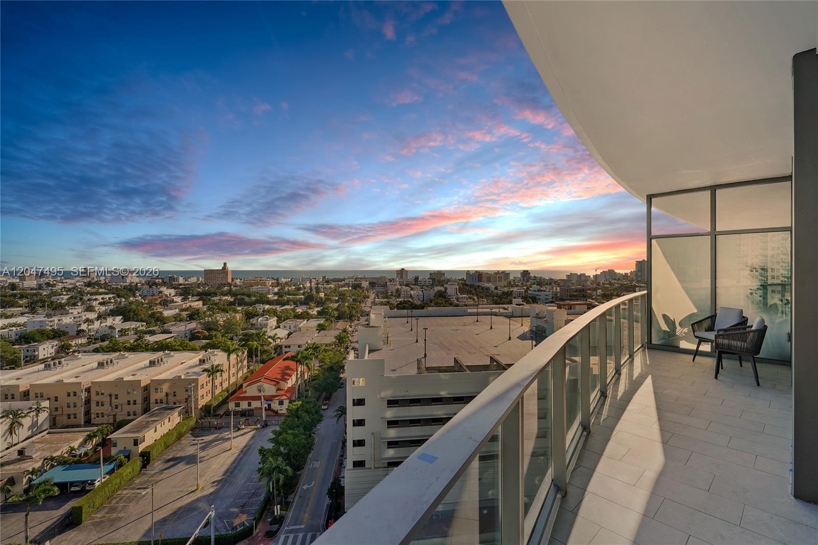 A high-rise balcony with a glass railing overlooks a city skyline at sunset — 500 Alton Rd # 1506, Miami Beach FL 33139, MIAMI BEACH, FL