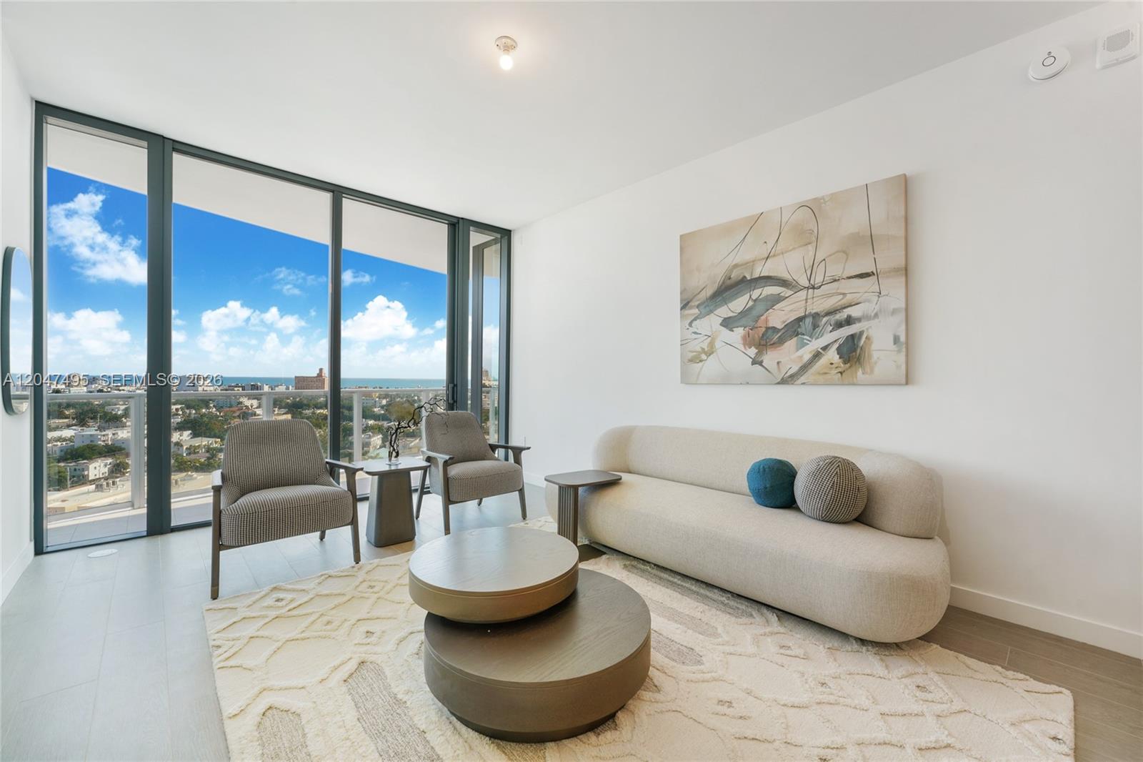 A modern living room features a curved sofa, two armchairs, and floor-to-ceiling windows with ocean views — 500 Alton Rd # 1506, Miami Beach FL 33139, MIAMI BEACH, FL