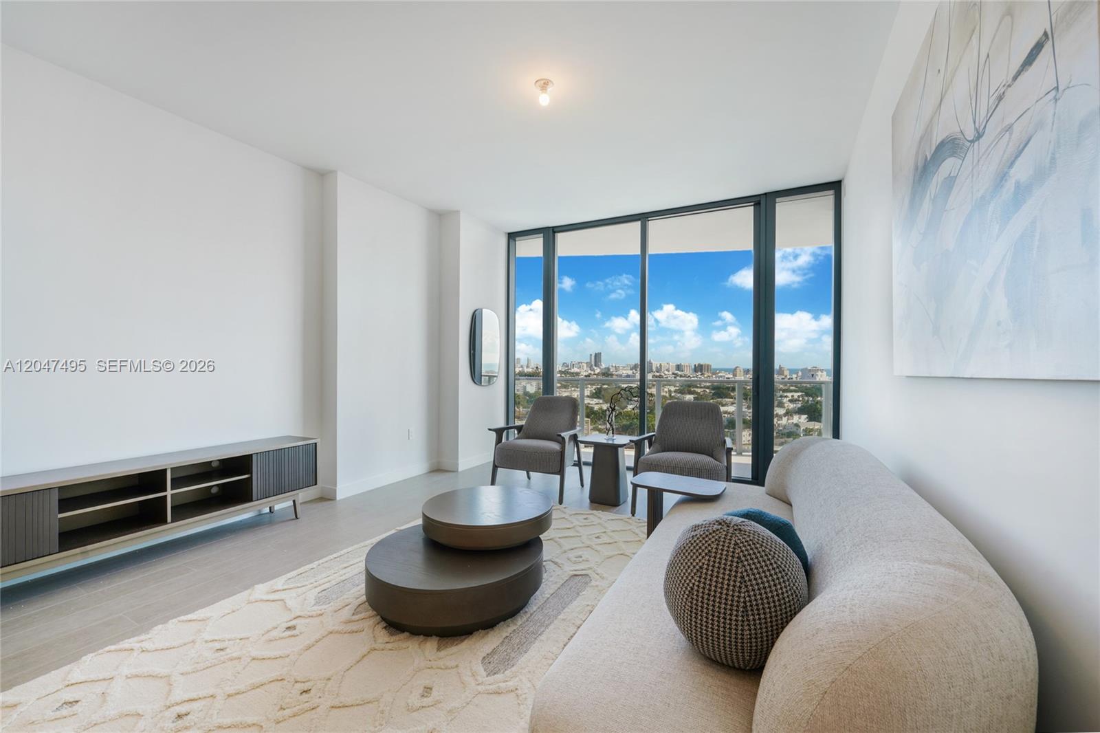 A modern living room features a curved sofa, two armchairs, and floor-to-ceiling windows with views — 500 Alton Rd # 1506, Miami Beach FL 33139, MIAMI BEACH, FL
