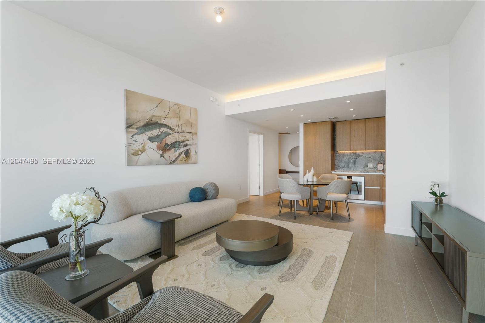A modern living room features a curved sofa, a circular coffee table, and an open kitchen — 500 Alton Rd # 1506, Miami Beach FL 33139, MIAMI BEACH, FL