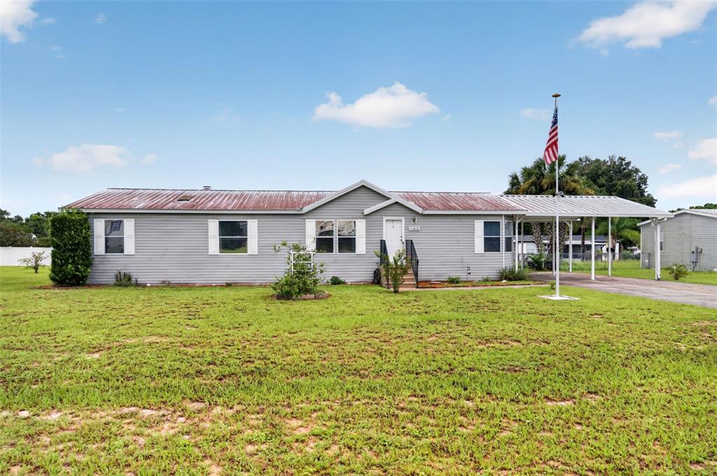 A single-story gray manufactured home with a metal roof, front porch, and attached carport — 11416 PHEASANT TRAIL, LEESBURG, FL