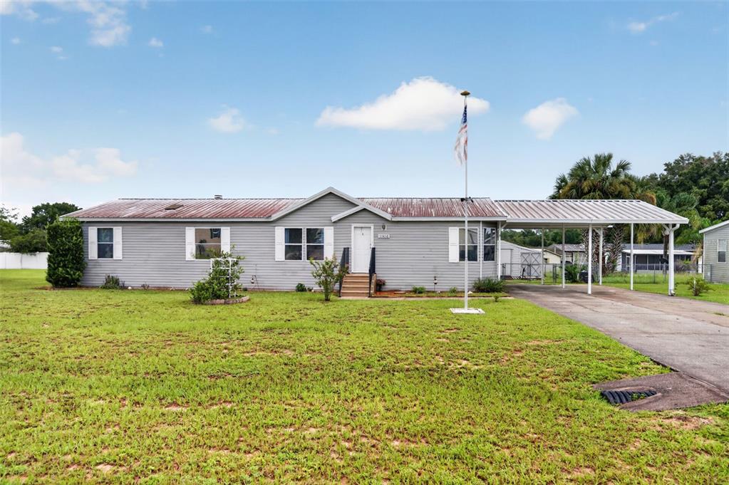 A single-story gray house with a metal roof, front porch, and an attached carport — 11416 PHEASANT TRAIL, LEESBURG, FL