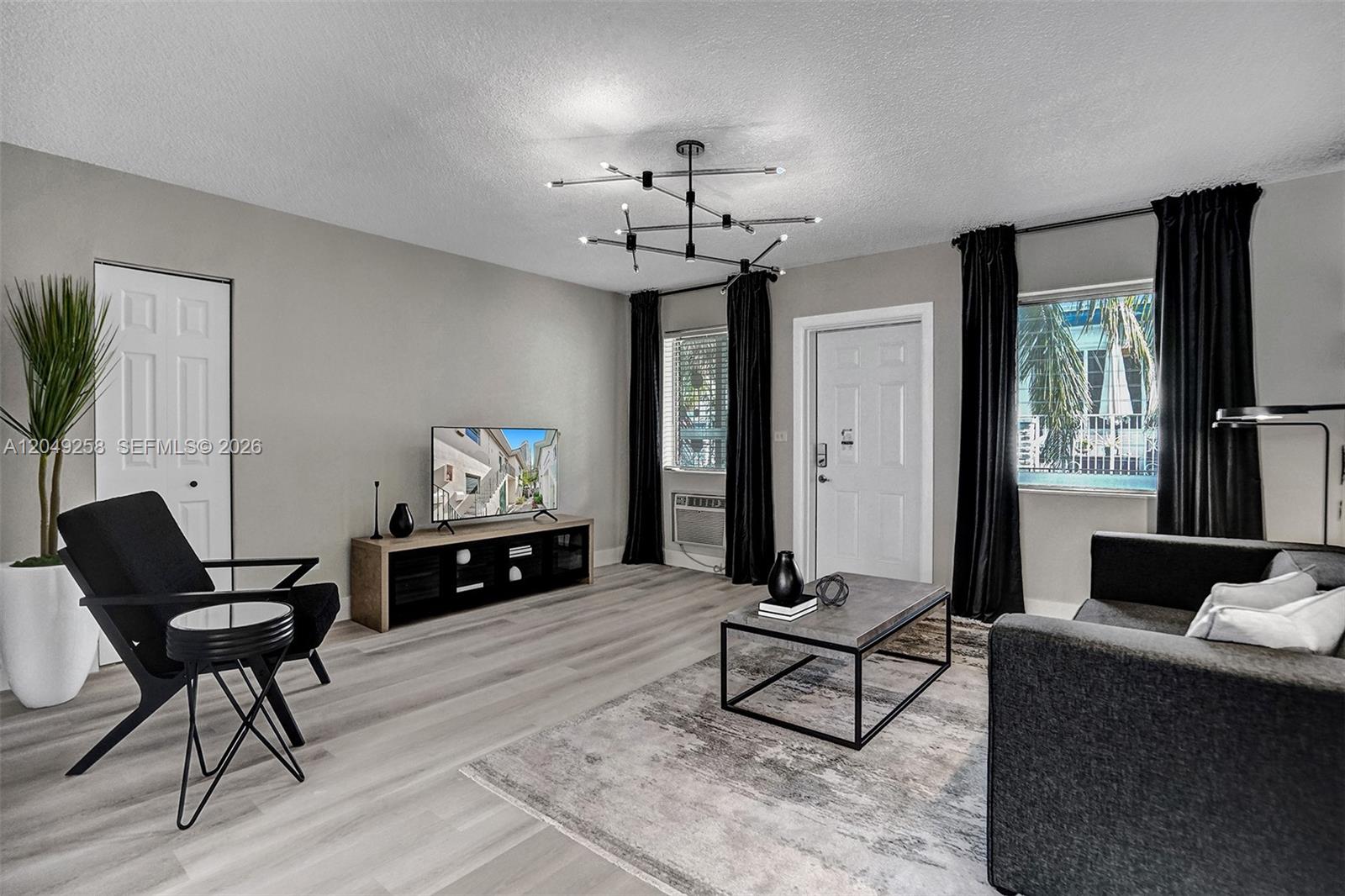 A modern living room features light wood floors, a black chandelier, and dark furniture — 1430 16th St # 1, Miami Beach FL 33139, MIAMI BEACH, FL