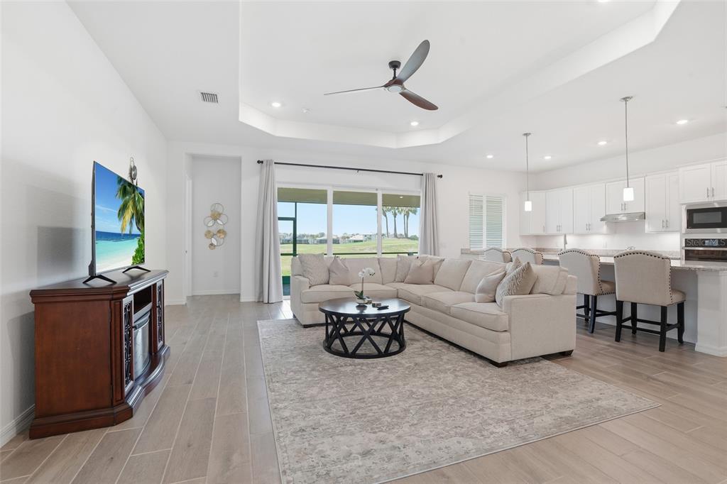 An open-concept living room and kitchen featuring a tray ceiling, tile floors, and sliding doors — 14413 HERITAGE LANDING BOULEVARD, PUNTA GORDA, FL