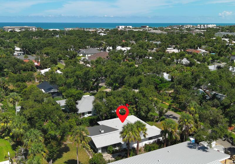 An aerial view shows a single-story house with a gray roof surrounded by lush trees — VERO BEACH, FL