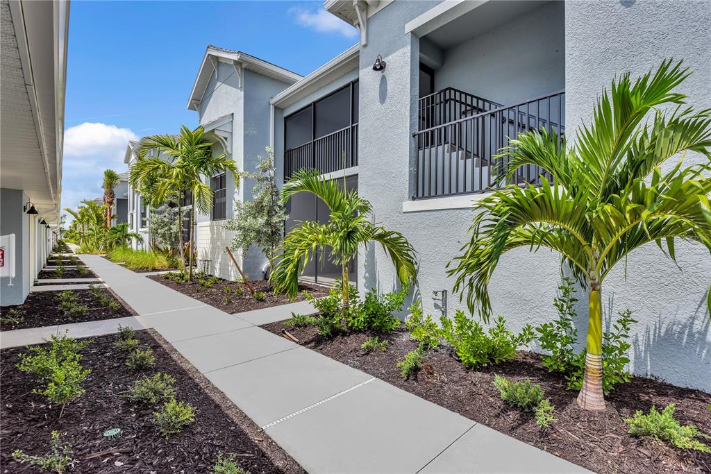 A sidewalk runs alongside a multi-story apartment building with palm trees and landscaped mulch beds — 14271 HERITAGE LANDING BOULEVARD UNIT 1527, PUNTA GORDA, FL