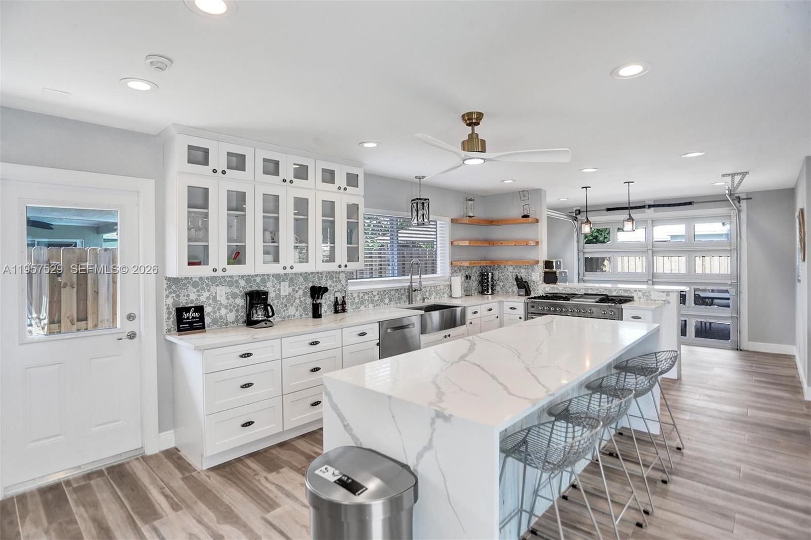 A modern kitchen features white cabinetry, a marble-topped island, and a glass-paneled garage door — 1341 SE 7th Ave, Pompano Beach FL 33060, POMPANO BEACH, FL