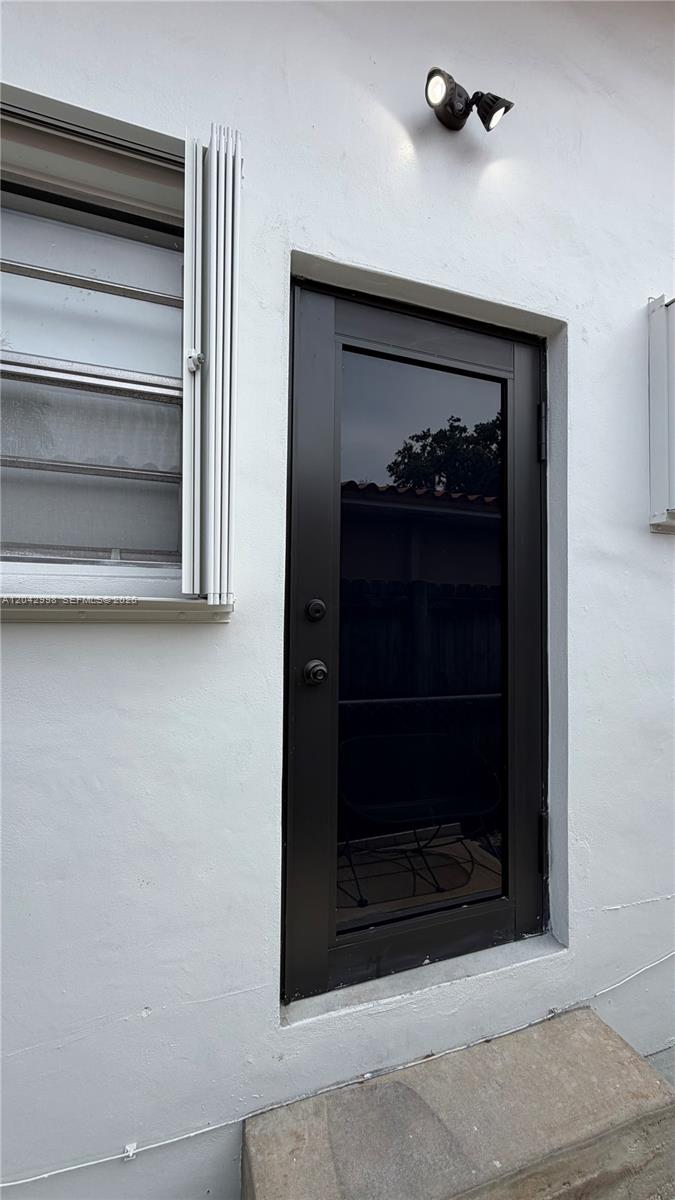A dark-framed glass door is set into a white exterior wall next to a window — 612 NW 43rd Ct # 0, Miami FL 33126, MIAMI, FL