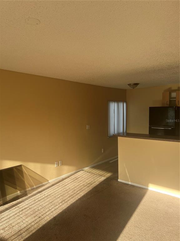 A living room with beige carpet and walls, featuring a kitchen counter and refrigerator — 800 N FISKE BOULEVARD UNIT 711, COCOA, FL