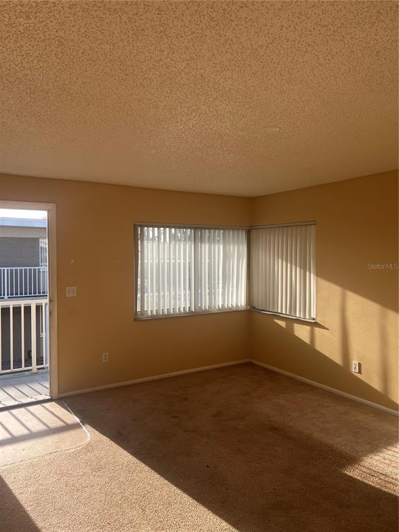 An empty room with beige carpet, tan walls, vertical blinds, and a balcony door — 800 N FISKE BOULEVARD UNIT 711, COCOA, FL