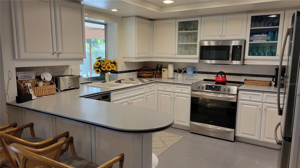A kitchen features white cabinetry, gray countertops, stainless steel appliances, and a breakfast bar — 638 S OWL DRIVE, SARASOTA, FL
