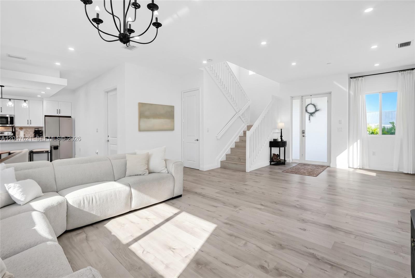 A bright living room features light wood flooring, a white sectional sofa, and a staircase — 17901 SW 152nd Ave, Miami FL 33187, MIAMI, FL