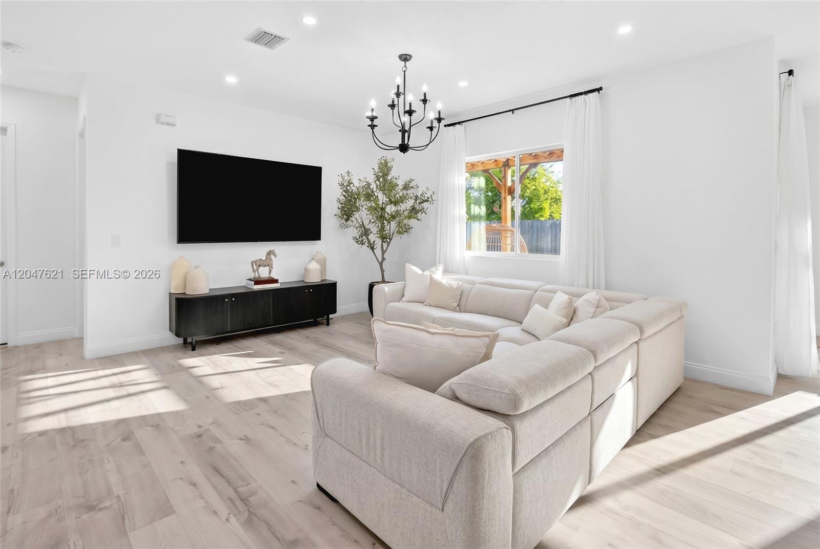 A bright living room features a large sectional sofa, a black media console, and chandelier — 17901 SW 152nd Ave, Miami FL 33187, MIAMI, FL