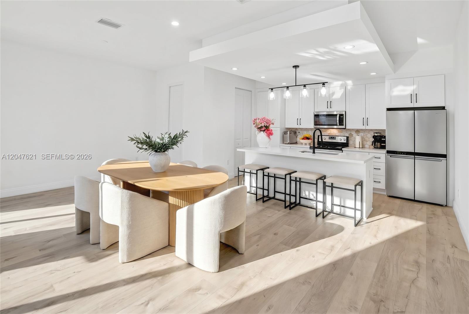 A modern kitchen and dining area feature white cabinetry, a central island, and light wood flooring — 17901 SW 152nd Ave, Miami FL 33187, MIAMI, FL