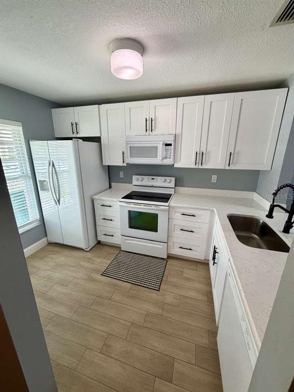 A kitchen features white cabinetry, stainless steel appliances, light countertops, and wood-look tile flooring — 2852 STILWELL COURT, NEW PORT RICHEY, FL