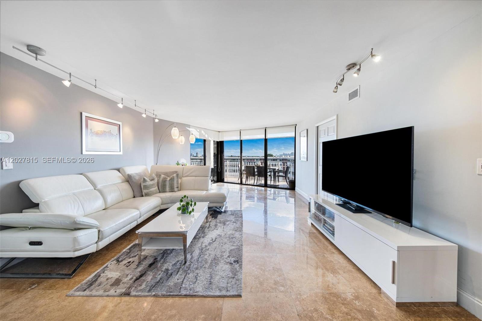 A living room features a white sectional sofa, a television, and a balcony with views — 4000 Towerside Ter # 604, Miami FL 33138, MIAMI, FL