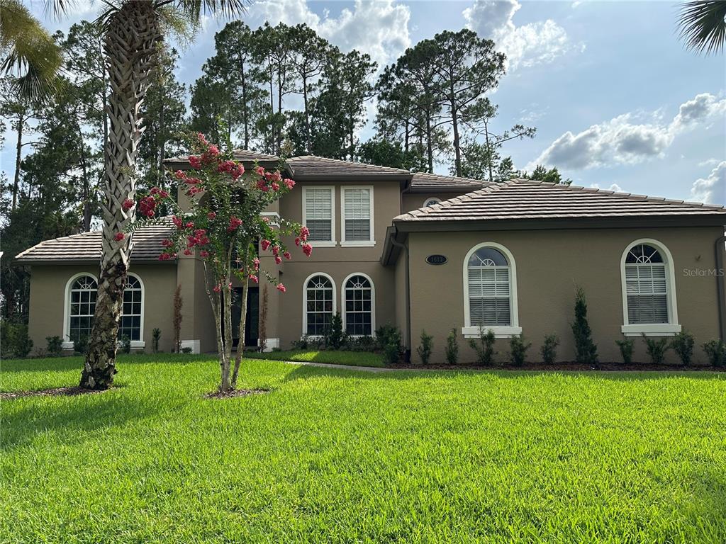 A two-story tan house with a tiled roof, arched windows, and a front lawn — 1613 SHADOWMOSS CIRCLE, LAKE MARY, FL