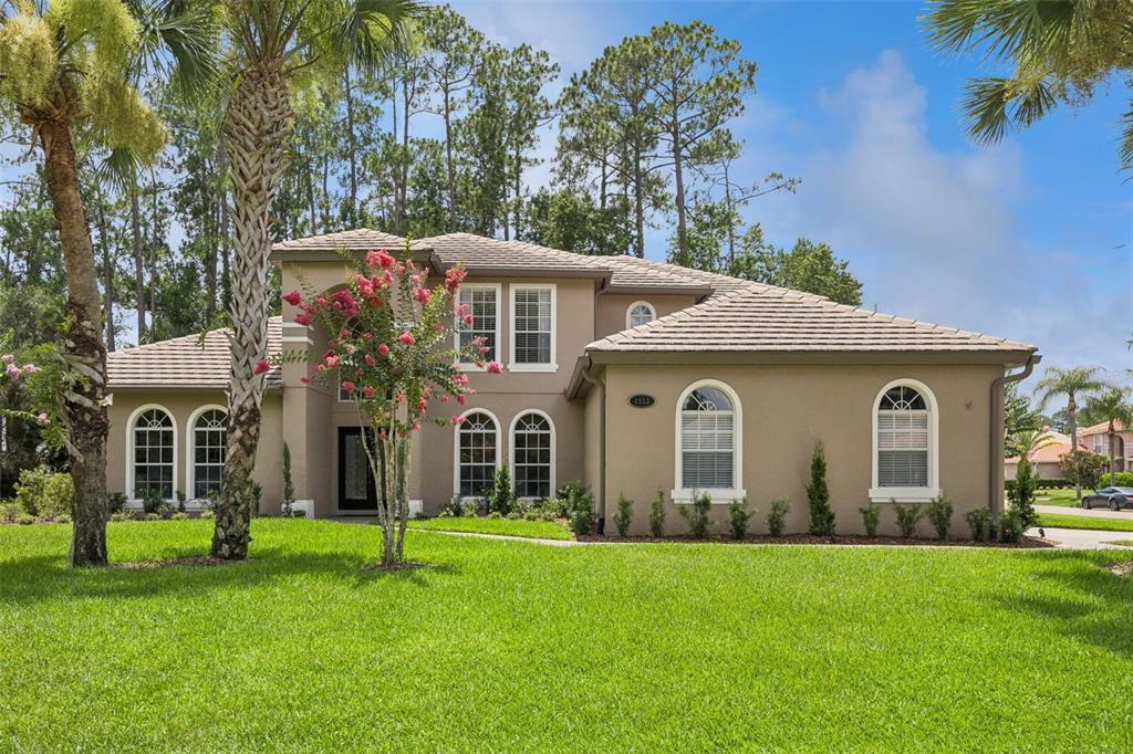 A two-story tan stucco house with a tiled roof and arched windows sits on grass — 1613 SHADOWMOSS CIRCLE, LAKE MARY, FL