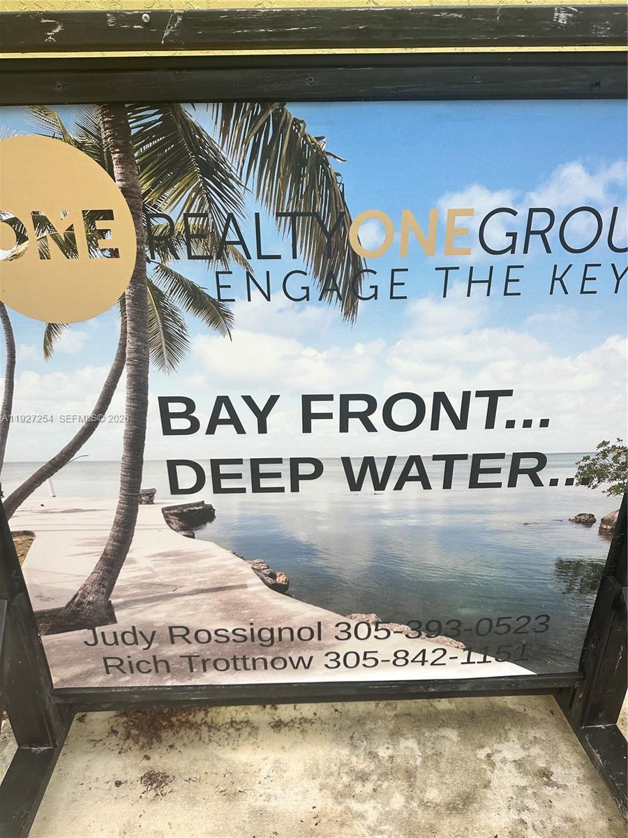 A real estate sign displays the text "BAY FRONT... DEEP WATER..." with two phone numbers — 166 Bayview Drive, Islamorada FL 33036, ISLAMORADA, FL