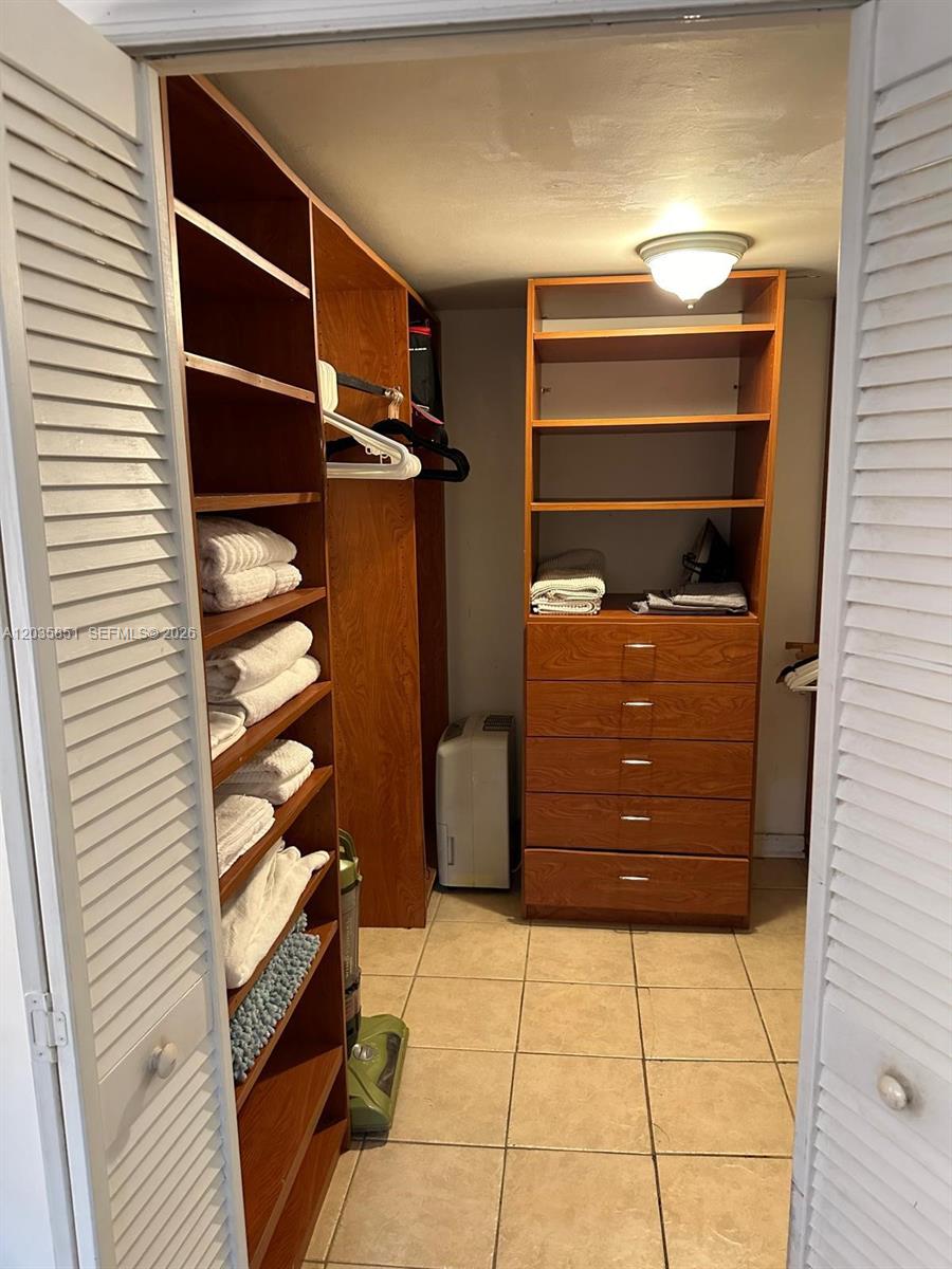 A walk-in closet features wooden shelving, a built-in dresser, and tiled flooring — 1515 West Ave # 1, Miami Beach FL 33139, MIAMI BEACH, FL