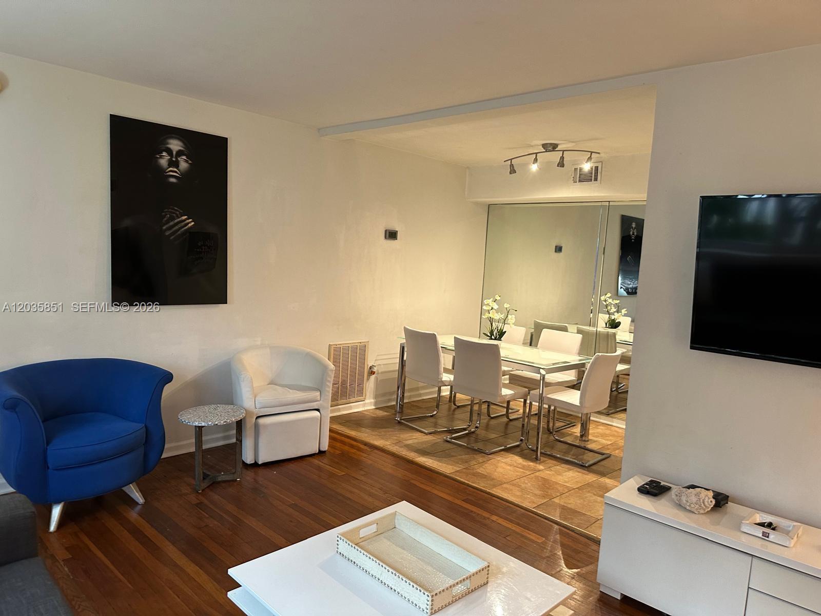A living room with a blue chair, white furniture, and an adjacent dining area with mirrors — 1515 West Ave # 1, Miami Beach FL 33139, MIAMI BEACH, FL
