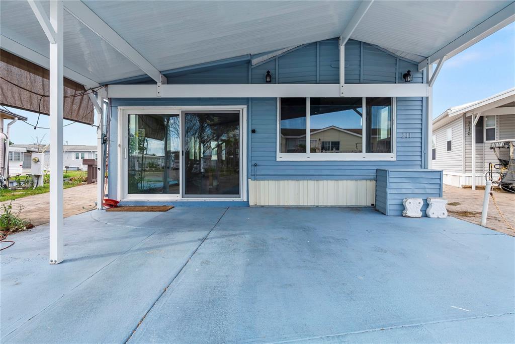 A blue mobile home exterior features a covered concrete patio, sliding glass doors, and windows — 9000 US HIGHWAY 192 UNIT 211, CLERMONT, FL
