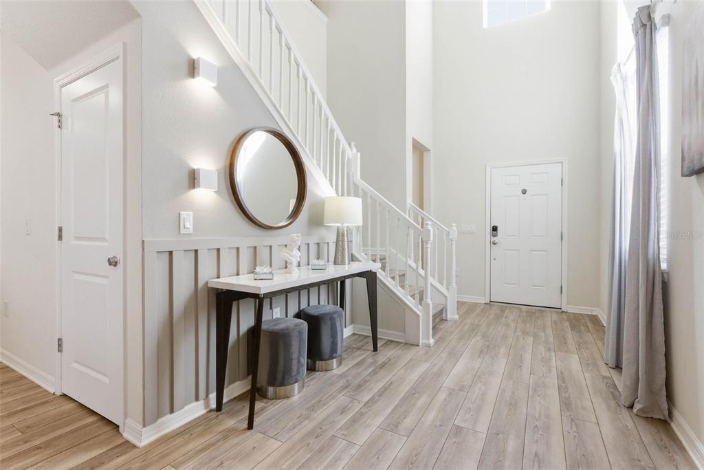 A bright entryway features a white staircase, wood-look flooring, a console table, and wall paneling — 1721 KONA LANE LANE, DAVENPORT, FL