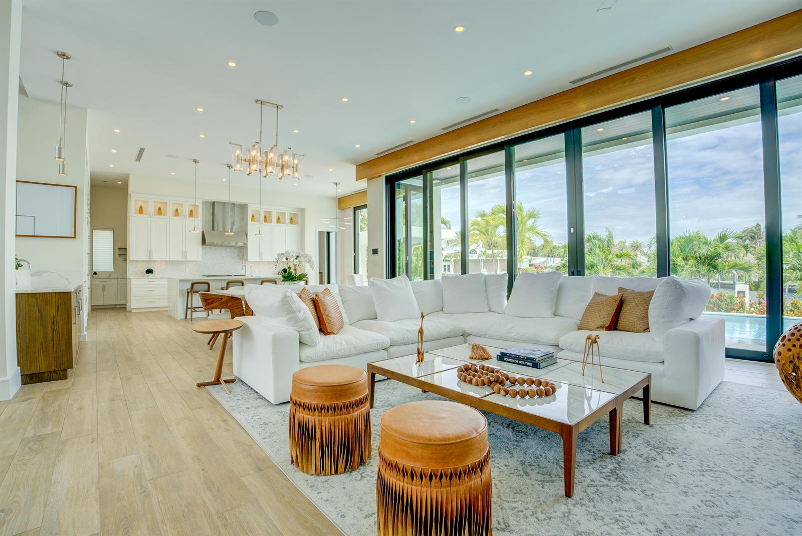 A bright, open-concept living room features a white sectional sofa, leather ottomans, and floor-to-ceiling windows — 2801 NE 36th Street, Lighthouse Point FL 33064, LIGHTHOUSE POINT, FL
