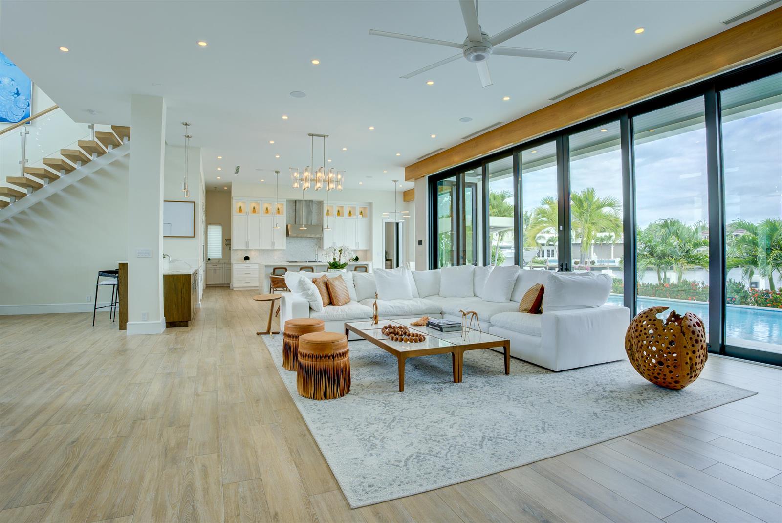 A modern open-concept living room features a white sectional sofa, wood-framed coffee tables, and floor-to-ceiling glass doors — 2801 NE 36th Street, Lighthouse Point FL 33064, LIGHTHOUSE POINT, FL