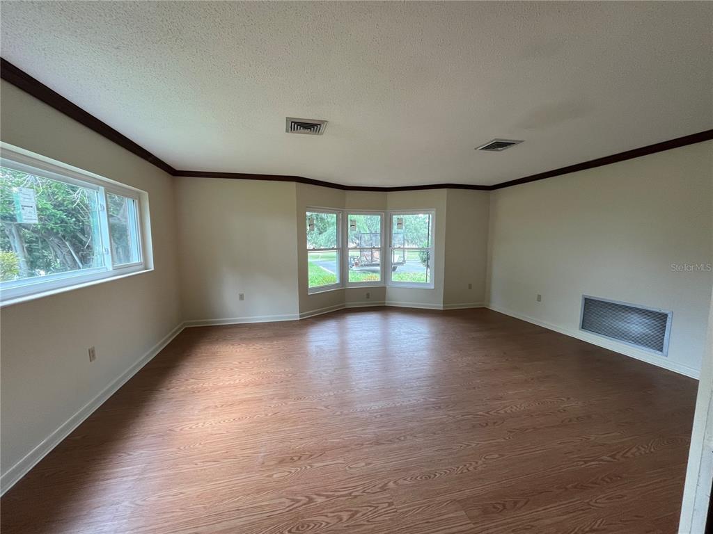 An empty living room features wood-look flooring, beige walls, a bay window, and crown molding — 1145 S LAKE REEDY BOULEVARD, FROSTPROOF, FL