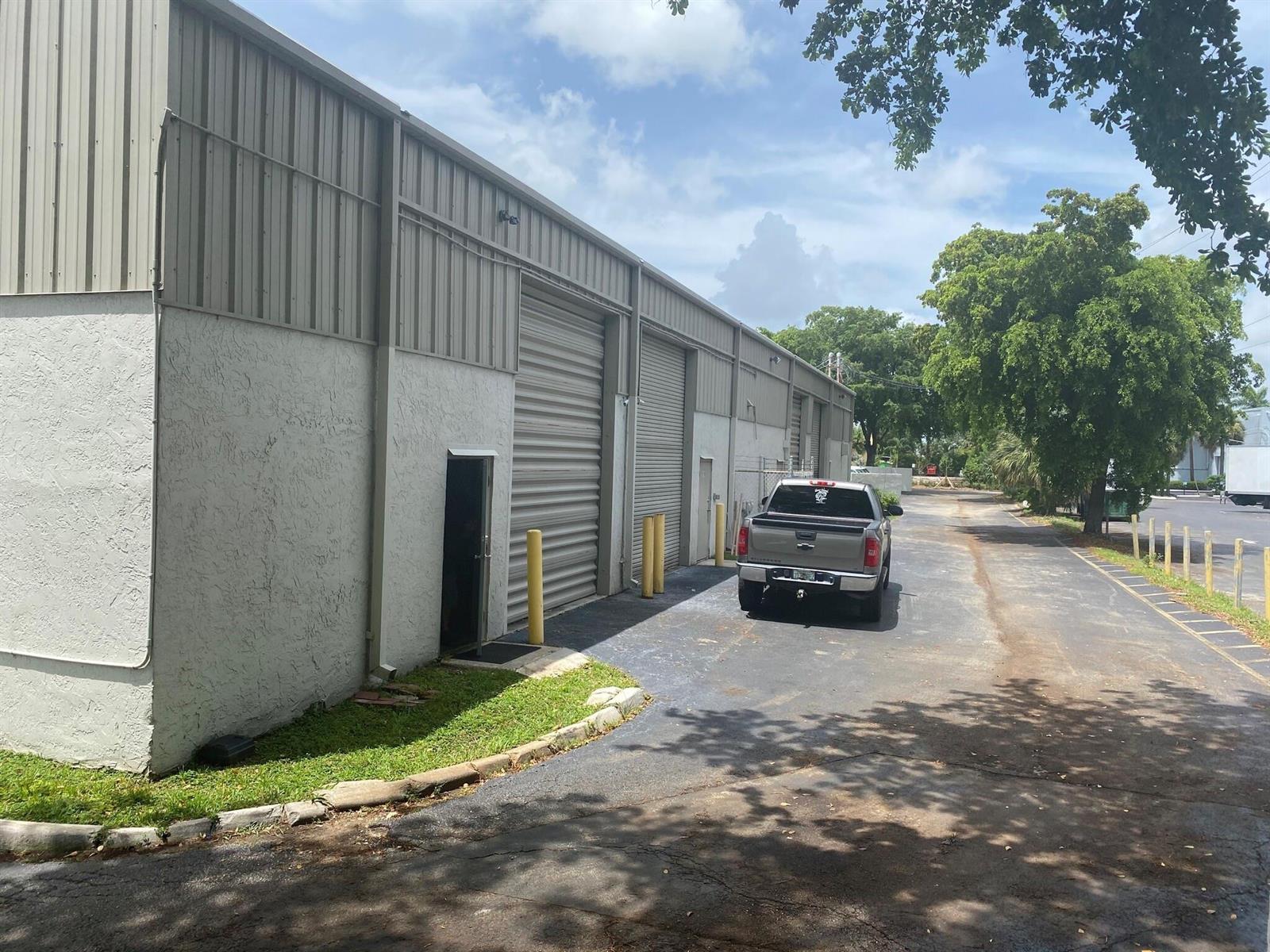 A gray pickup truck is parked in front of a warehouse building with metal roll-up doors — 290 SW 12th Avenue, Pompano Beach FL 33069, POMPANO BEACH, FL