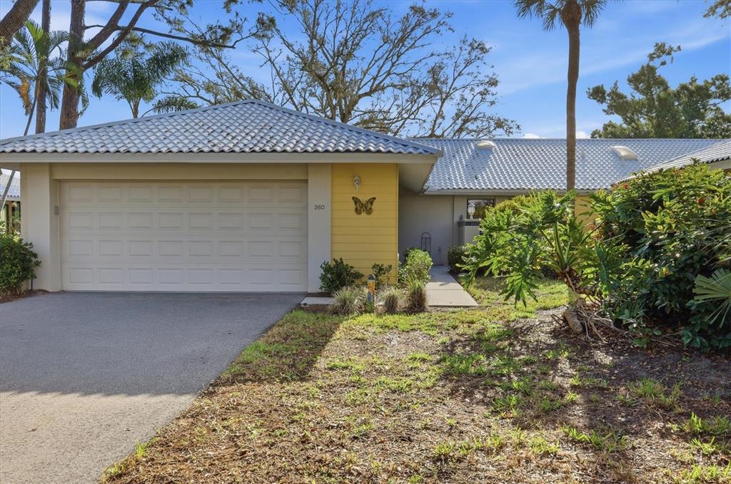A single-story house features a yellow garage wall, a white tiled roof, and landscaping — 260 SOUTHAMPTON DRIVE UNIT 312, VENICE, FL