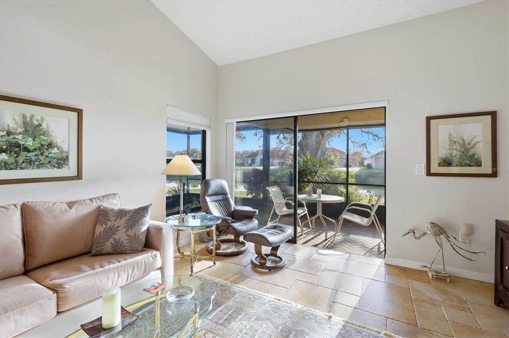 A living room with tile floors, a sofa, a recliner, and a sliding glass door — 260 SOUTHAMPTON DRIVE UNIT 312, VENICE, FL