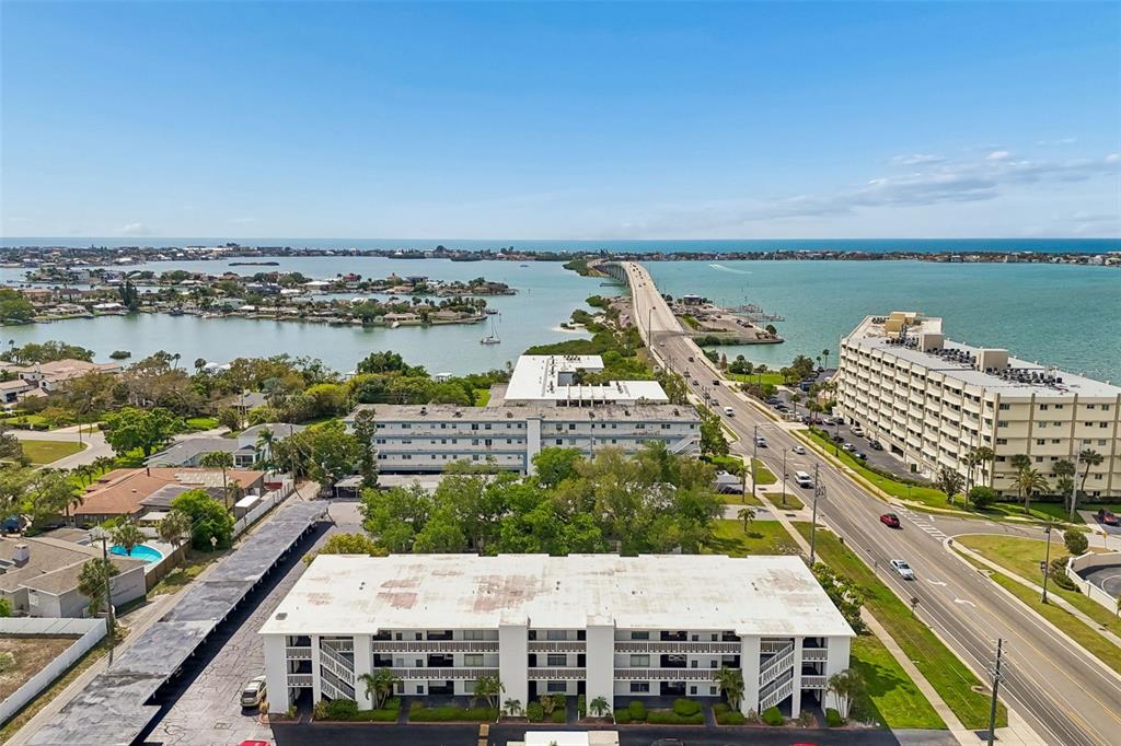 An aerial view shows multi-story apartment buildings, a coastal road, and a bridge over water — 2944 W BAY DRIVE UNIT 106, BELLEAIR BLUFFS, FL