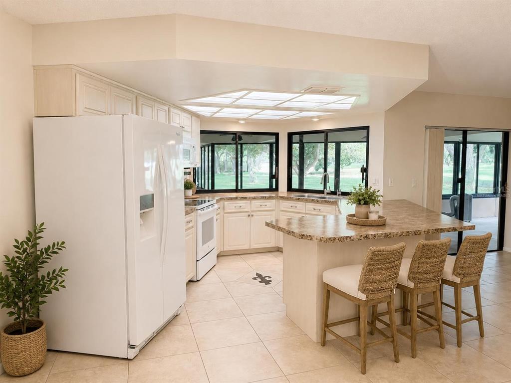 A kitchen with white cabinets, a stone-topped island, and a large window overlooking a yard — 2721 NORTHRIDGE DRIVE E, CLEARWATER, FL