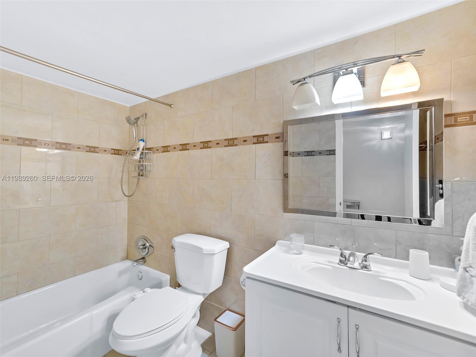 This bathroom features a white vanity, a toilet, and a bathtub with beige tiled walls — 3140 S Ocean Dr # 612, Hallandale Beach FL 33009, HALLANDALE BEACH, FL